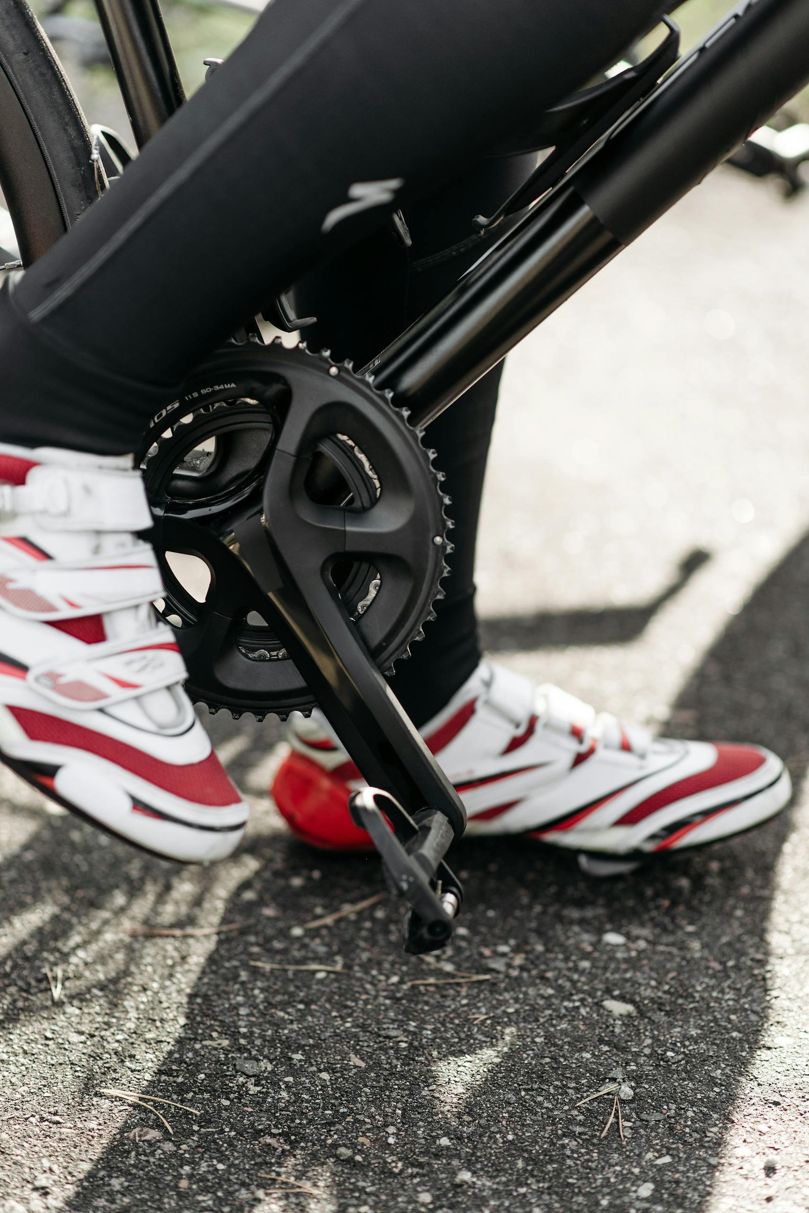 Close-up view of a cyclist's pedal and red-white cleats on asphalt.
