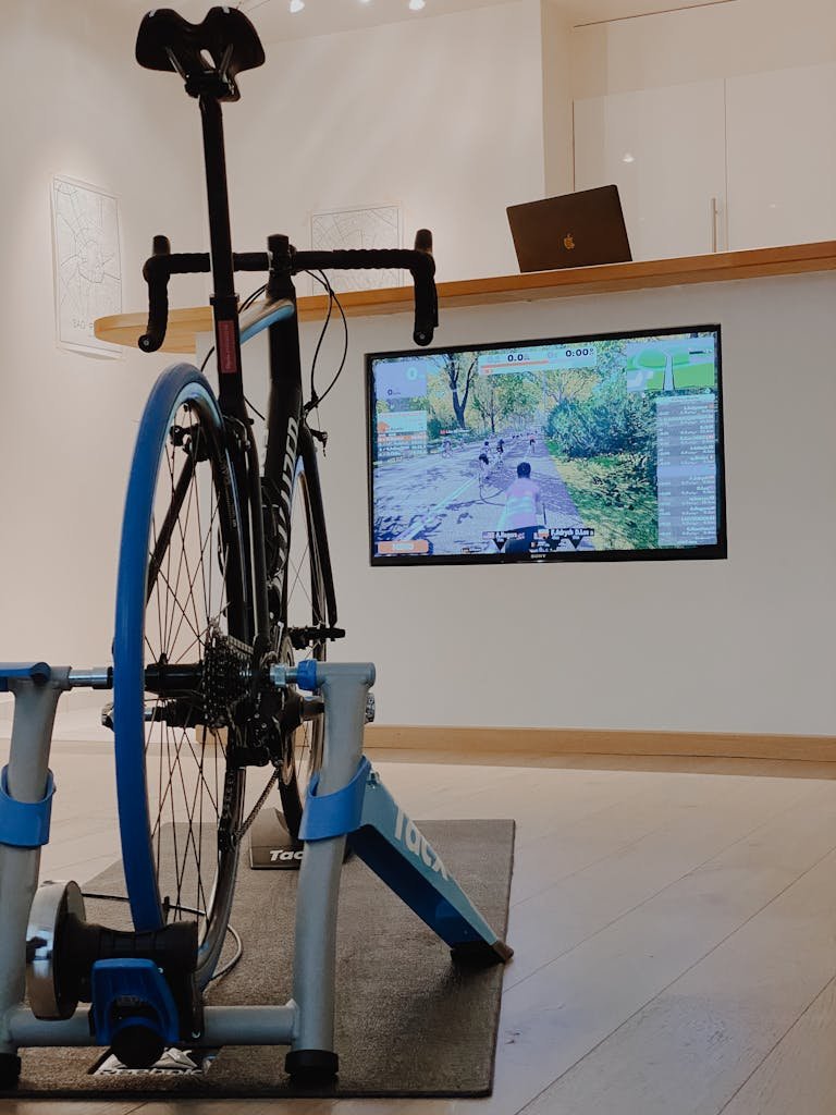 Photo by Flo Dahm Home cycling setup showing a bike on a trainer with a virtual cycling app on screen.