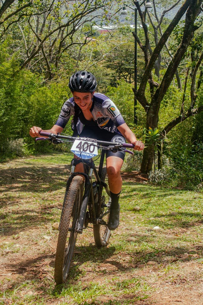 Photo by Jeferson Gonzalez Teenage girl cycling in a race through a scenic forest trail, smiling and enjoying the sport.