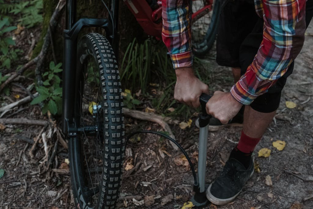 Photo by Anastasia Shuraeva A cyclist uses a pump to inflate a bicycle tire while in a forested area.