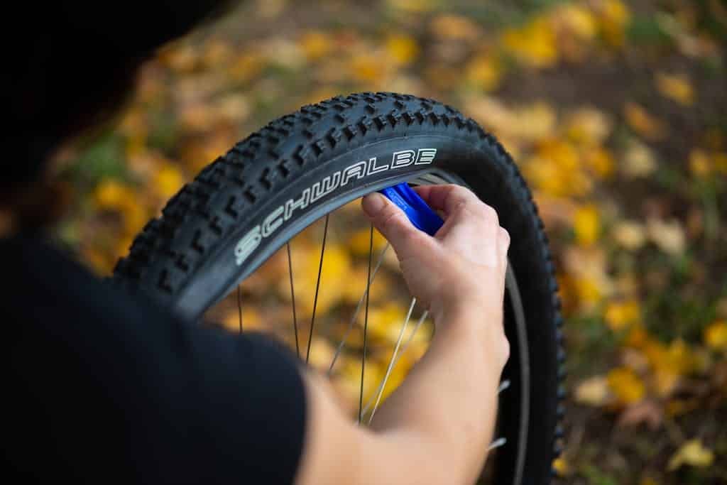 Photo by Rehook Bike A person repairing a bicycle tire outdoors with fallen autumn leaves in the background.