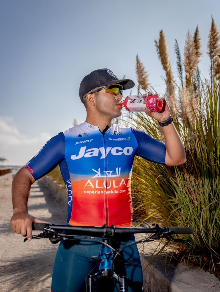 Photo by jose luis Umana A sportsman in team gear drinks from a bottle while cycling outdoors in Alto Hospicio, Chile.