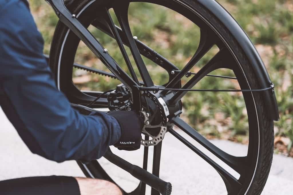 Photo by Motor TruckRun Close-up of a man fixing a bicycle wheel outdoors, showcasing mechanical details and tools.