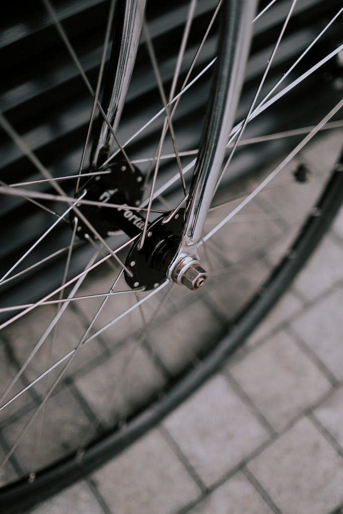 Detailed close-up of a chrome bicycle wheel showing spokes, hub, and rim on a cobblestone surface.