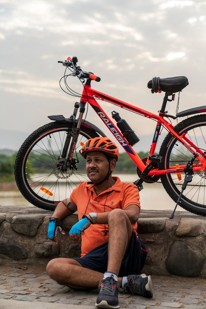 Photo by Nishant Aneja Man in sportswear resting by his bicycle outdoors, showcasing a lifestyle of leisure and fitness.