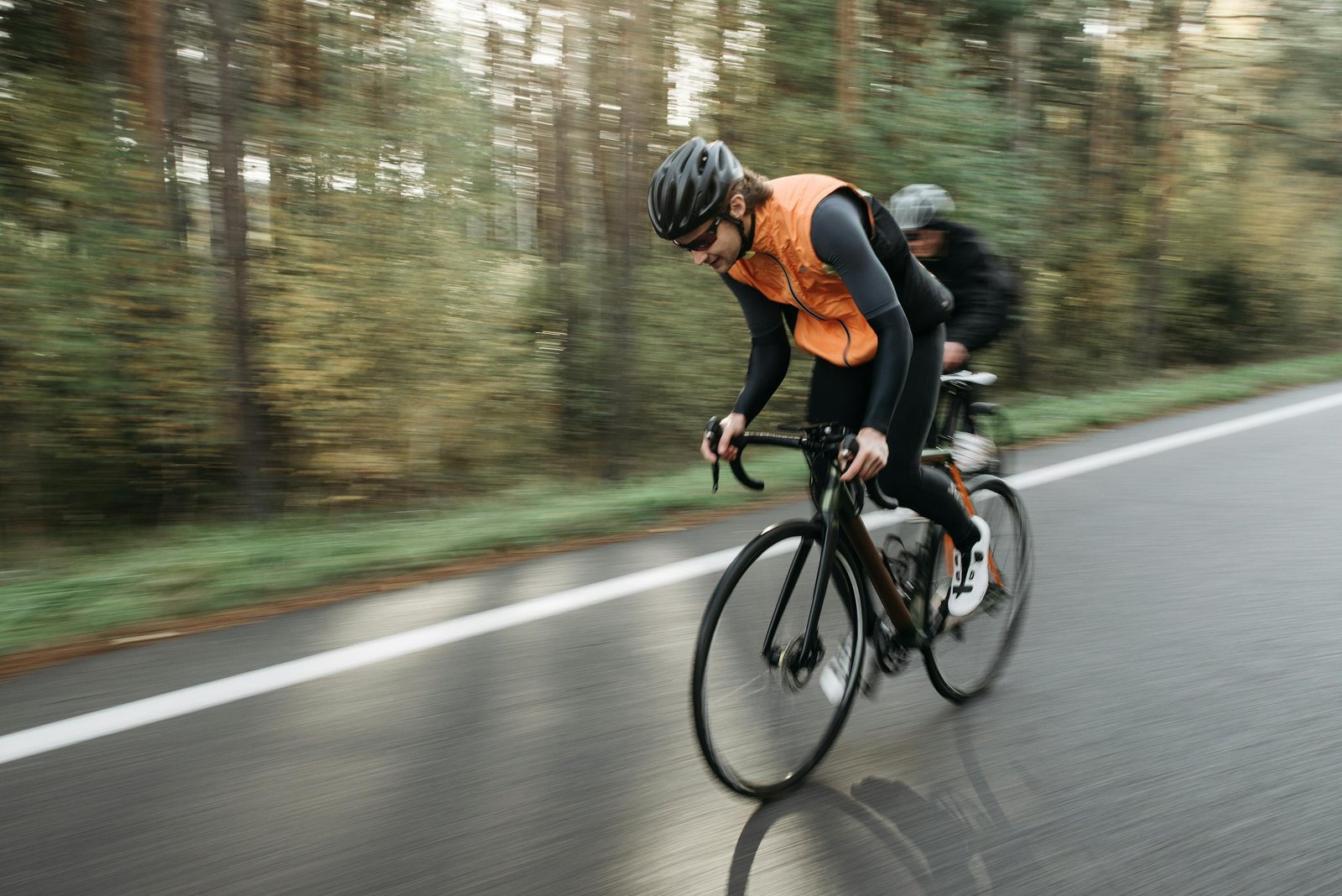 Two cyclists in activewear racing on an open road through a forest, showcasing speed and focus.