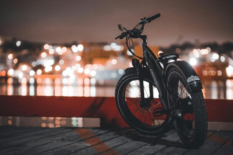 A bicycle parked by the waterfront at night with bokeh city lights in the background.