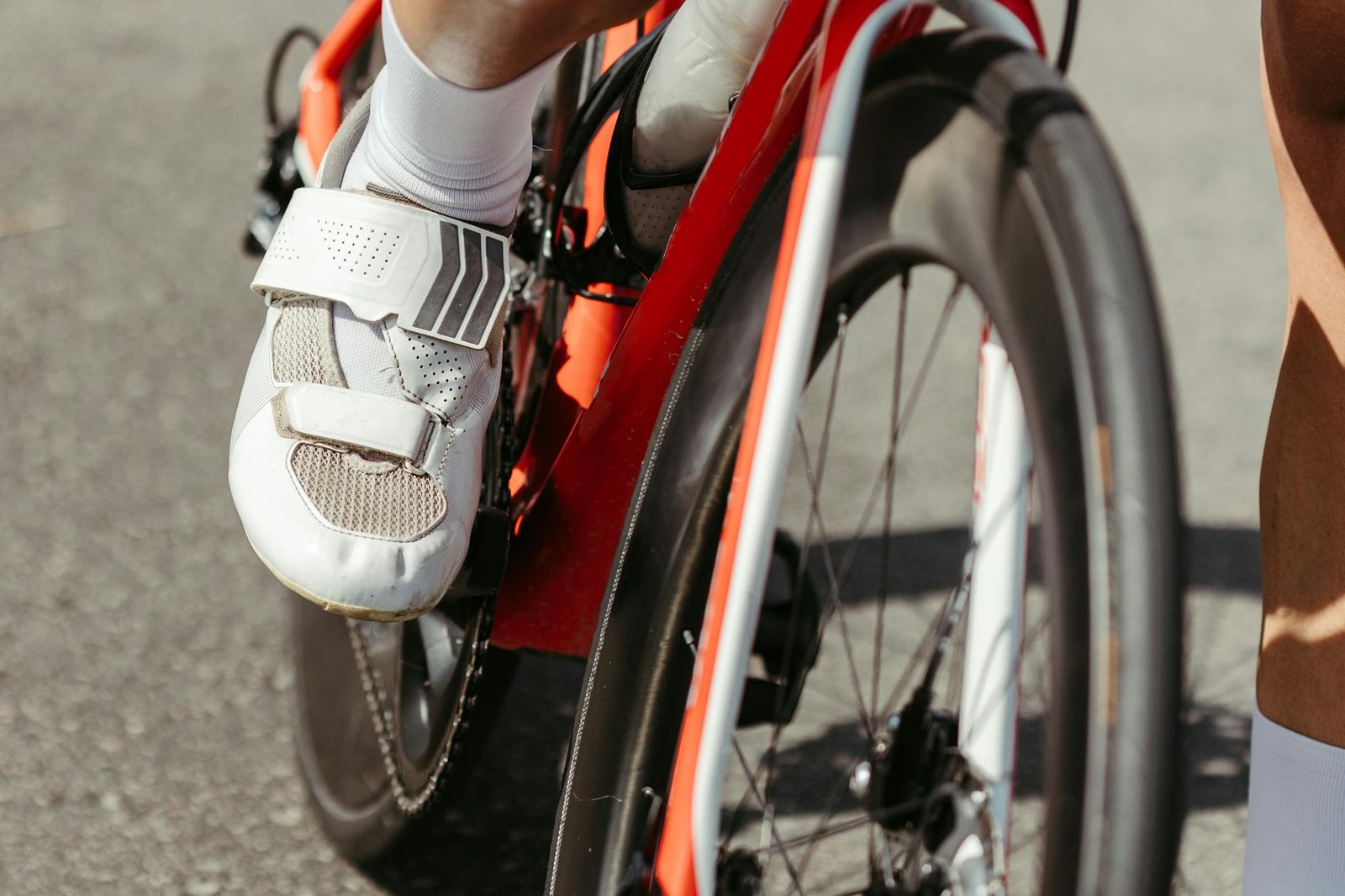 Detailed view of a cyclist's foot in white cycling shoe on a red racing bike pedal.