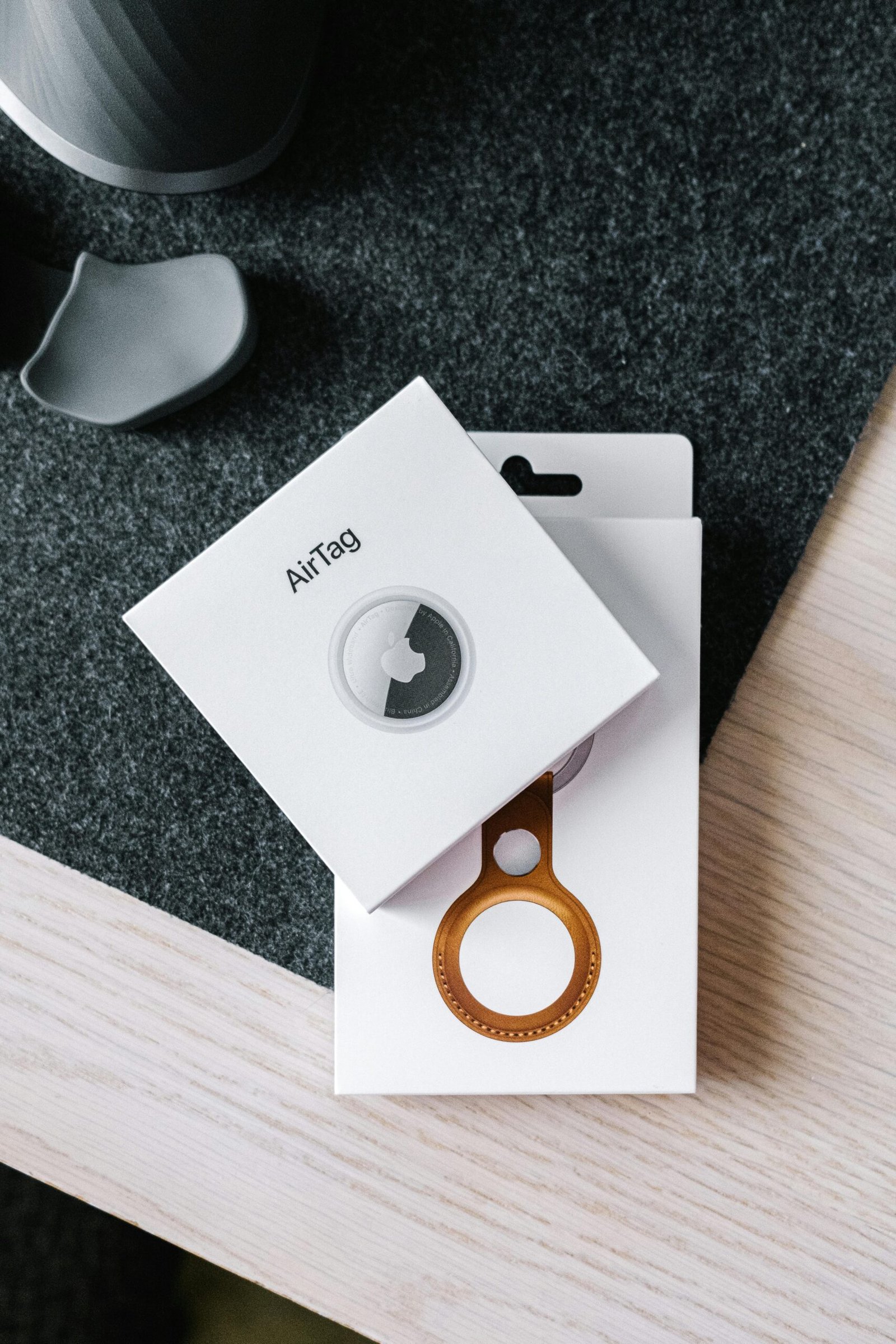 Overhead shot of AirTag and leather key ring packaging on wooden surface.