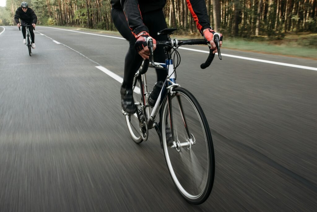 pexels-photo-5807613-5807613 Cyclists racing on an open road surrounded by nature, showcasing speed.